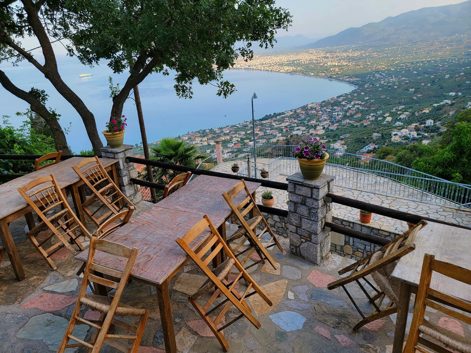 A taverna terrace with wooden tables overlooking a Greek bay